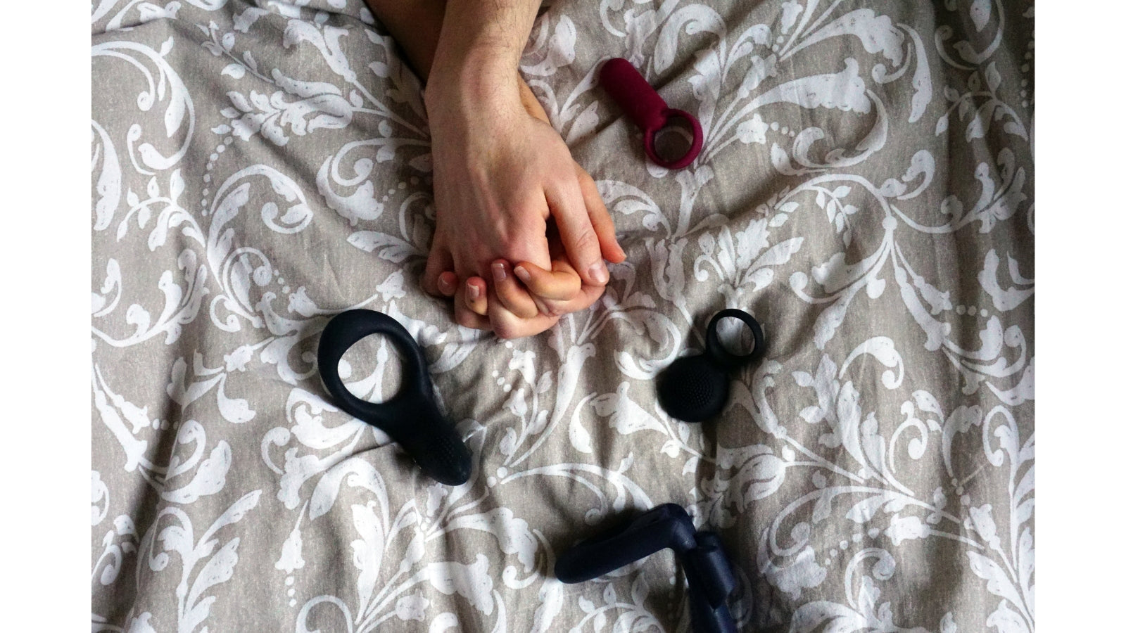 Deux mains enlacées sur un drap avec des sextoys autour