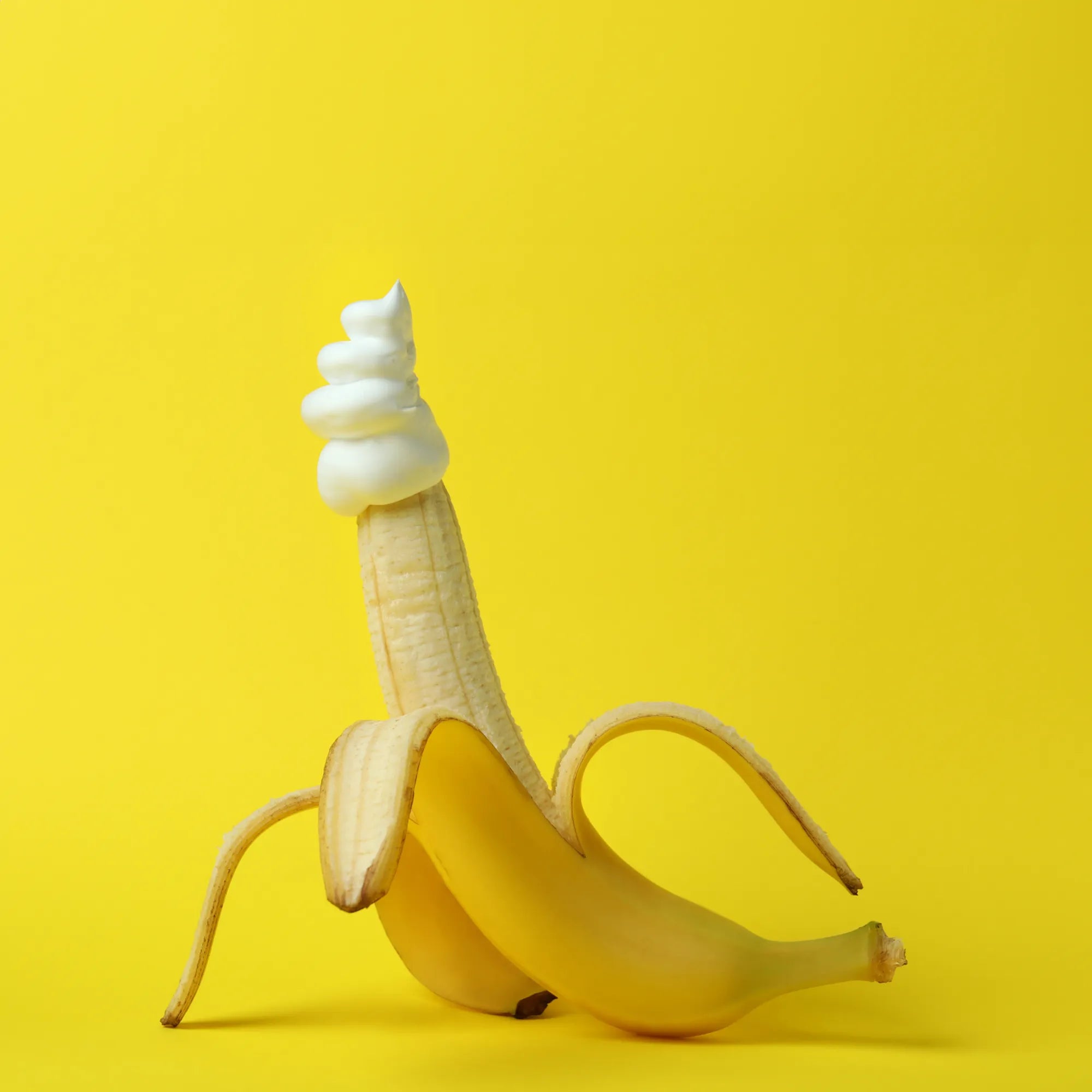 Banane épluchée avec crème fouettée sur le bout, fond jaune