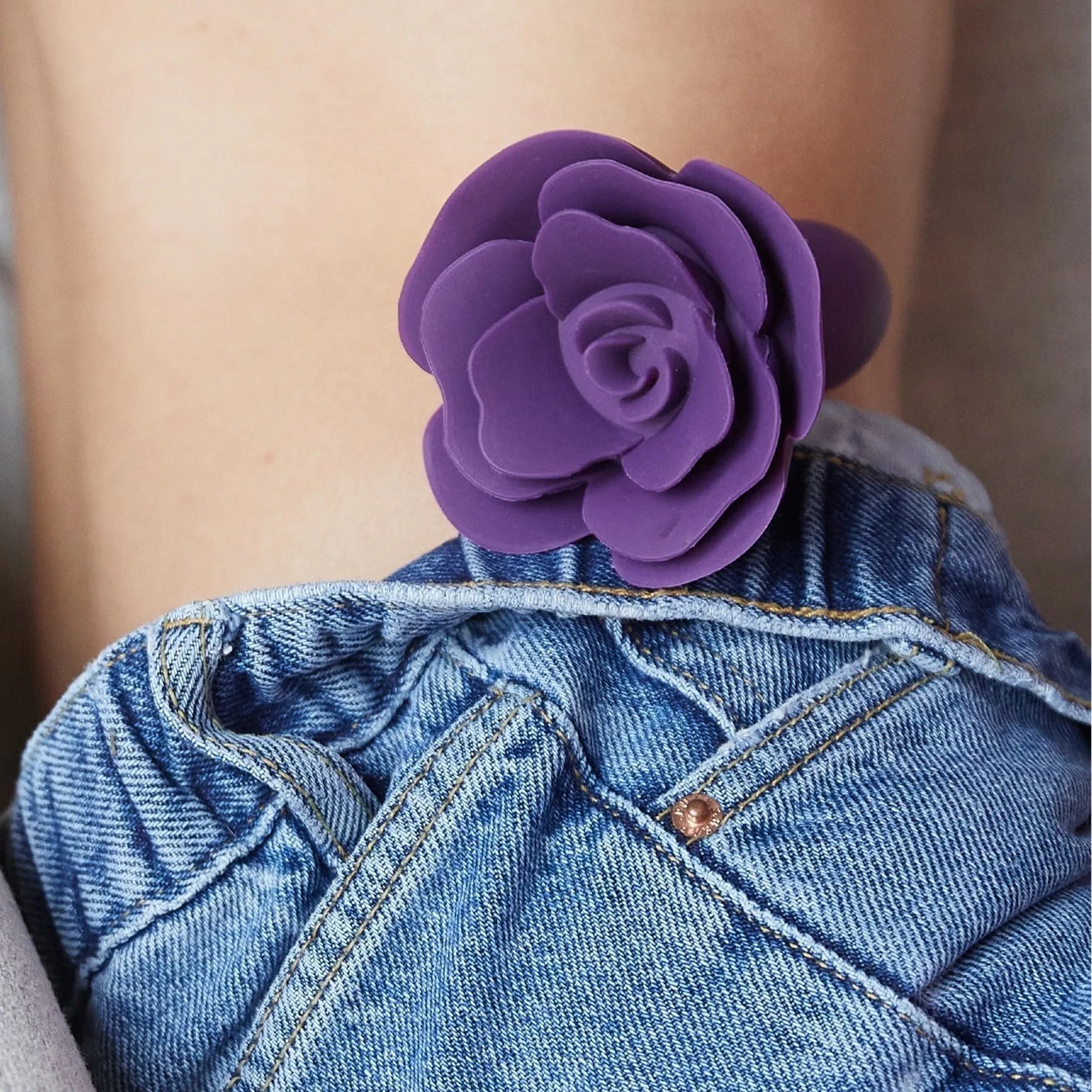 Plug anal en silicone violet Open Roses inséré avec base en forme de rose visible au-dessus d’un short en jean