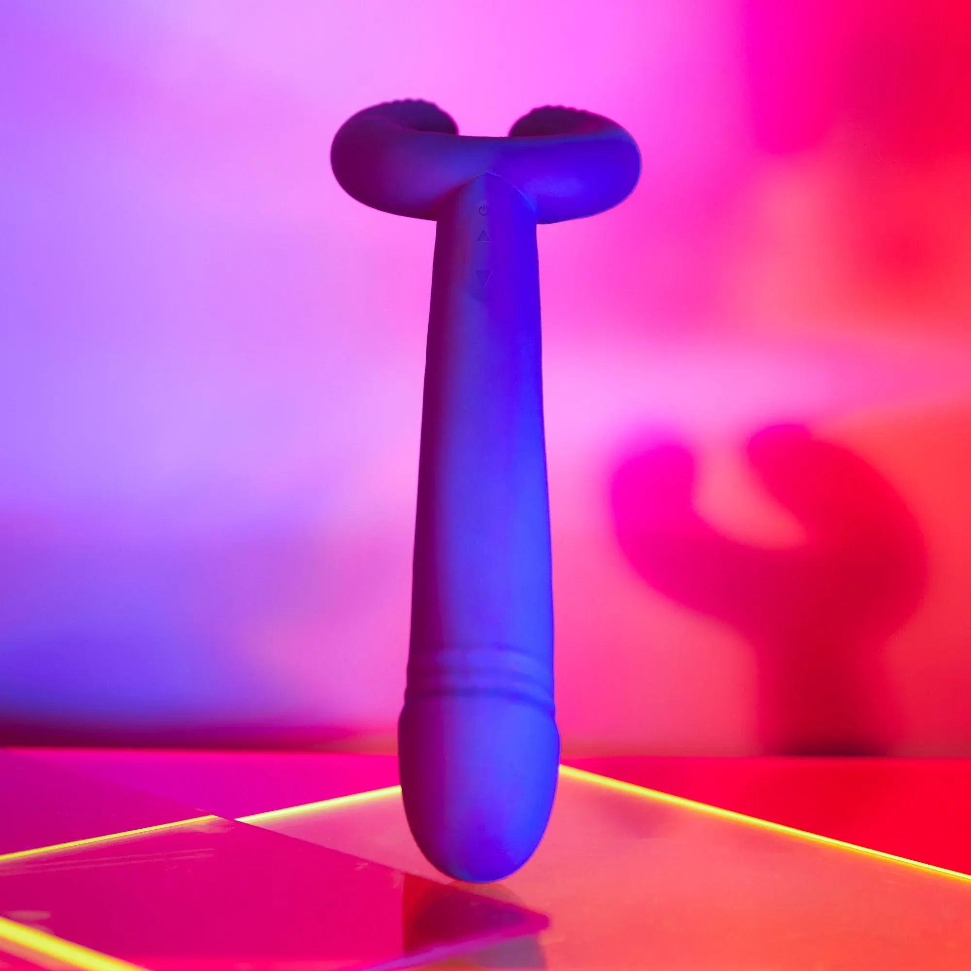 Le stimulateur Please Me Midnight Indigo mis en avant avec un éclairage coloré et une ombre projetée en arrière-plan.