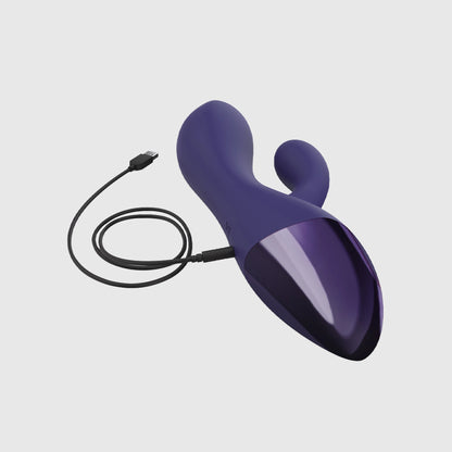 Vibromasseur rabbit flexible double stimulation Funky Bunny en silicone violet foncé avec finition métallisée, branché à son câble de recharge USB.