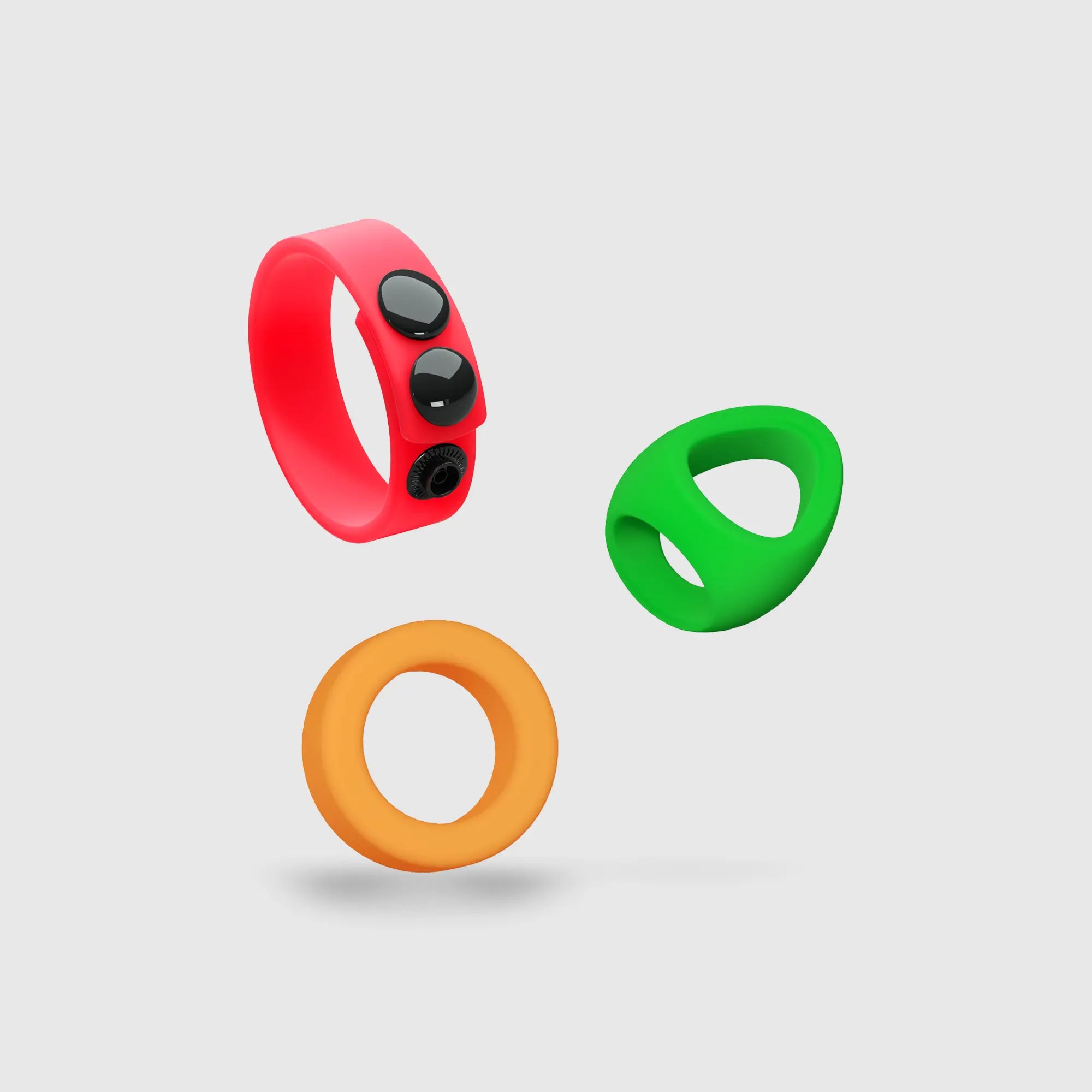 Trois anneaux péniens en silicone du Kit Neon Ring (rouge, vert, orange), flottant pour illustrer leur design coloré