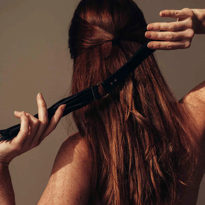 Femme tenant le fouet BDSM MAZE noir près de ses cheveux, suggérant un jeu de sensualité et de soumission