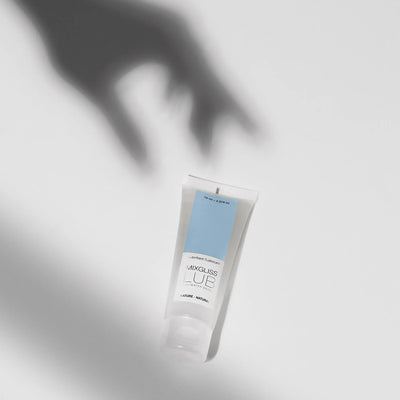 Ombre de main tendue vers un tube de lubrifiant Mixgliss posé à la verticale, effet artistique flouté.